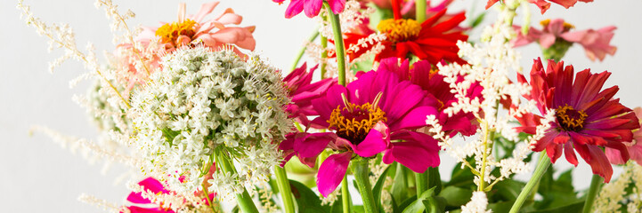 Summer bouquet of colorful Zinnia, onion inflorescences and mint sprigs, bouquet of flowers on the table near the wall, home decoration with flowers banner