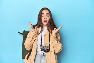 Young Caucasian woman traveler with camera and backpack surprised and shocked.