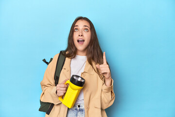 Adventurous woman with flashlight and backpack ready to explore pointing upside with opened mouth.