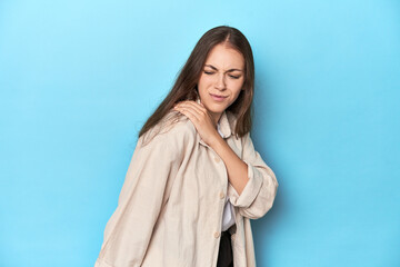 Naklejka premium Stylish young woman in an overshirt on a blue background having a shoulder pain.