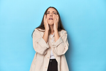 Stylish young woman in an overshirt on a blue background whining and crying disconsolately.