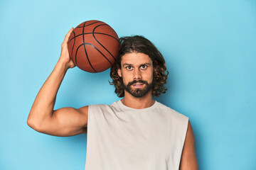 Long-haired, bearded man holding a basketball in a blue studio.