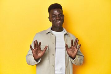 Stylish young African man on vibrant yellow studio background, rejecting someone showing a gesture...