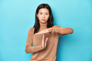 Young Asian woman in brown turtleneck, showing a timeout gesture.