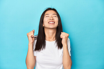 Young Asian woman in white t-shirt, studio shot, celebrating a victory, passion and enthusiasm, happy expression.