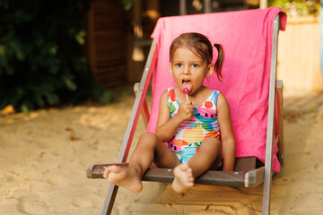 Funny cute girl on summer vacation. The child has fun on the beach. Cute baby girl in a colorful swimsuit is resting.
