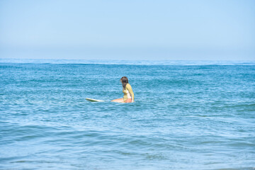 Pretty young woman sitting on her surfboard waiting for a wave
