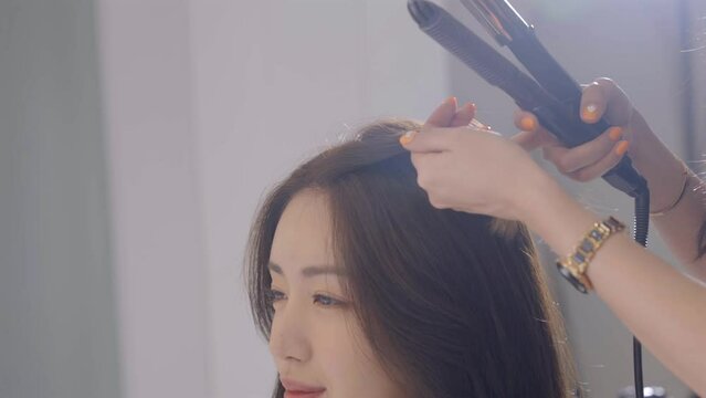 헤어샵에서 고데기를 사용하여 손님의 머리카락을 스타일링하는 헤어디자이너 