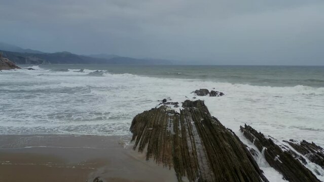 Thin sharp layered rocks extend into ocean, flysch itzurun zumaia spain, aerial reverse dolly