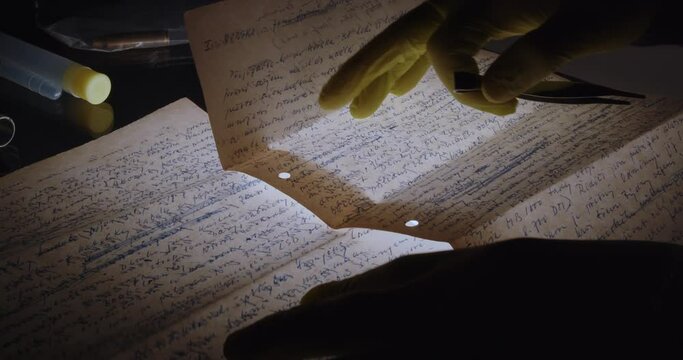 A forensic technician wearing gloves carefully studies handwritten letters
