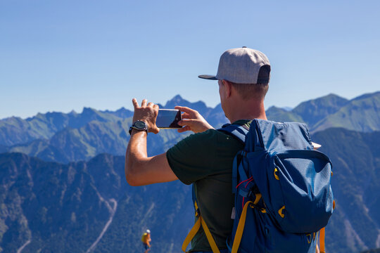 Wandern in den Allgäuer Alpen: Wanderer auf dem Gipfel der Kanzelwand, 2059 M. ü. M., fotografiert mit seinem Smartphone das Bergpanorama