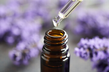 A drop of essential oil falling into a bottle, with purple lavender flowers