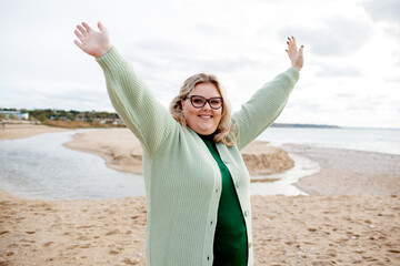 Beautiful woman walking in the sand beach in cold weather. Overweight model have fun . The happy girl wearing knit polluver. The plus size girl raised her hands up