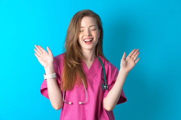 Emotive Young caucasian doctor woman wearing pink medical uniform laughs loudly, hears funny joke or story, raises palms with satisfaction,