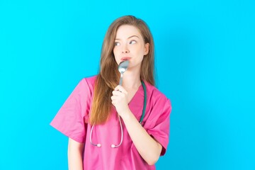 Very hungry Young caucasian doctor woman wearing pink medical uniform holding spoon into mouth...