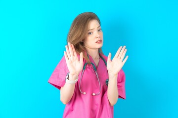 Young caucasian doctor woman wearing medical uniform Moving away hands palms showing refusal and...
