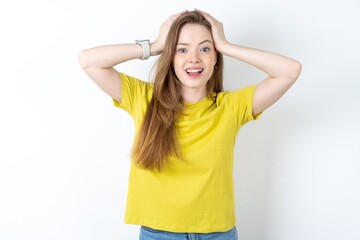 Obraz na płótnie Canvas Cheerful overjoyed Young beautiful girl wearing yellow T-shirt reacts rising hands over head after receiving great news.