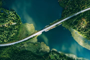  Aerial view of bridge asphalt road with cars and blue water lake and green woods in Finland. © nblxer