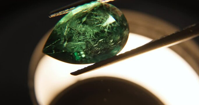 Close up shot of emerald green gemstone under microscope held by tweezers. Gemmological laboratory. Gem grading and valuation