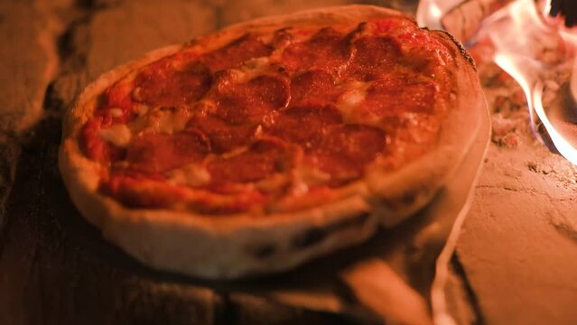 Italian pizza pepperoni is cooked in a wood-fired oven. Pizza with salami in hot oven close up. Food video. UHD 4k video