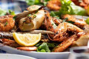 Grilled seafood on a plate in a restaurant. A dish of shrimp, squid, fish and greens - obrazy, fototapety, plakaty