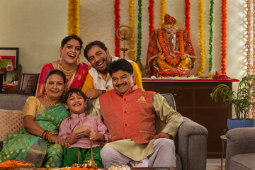 Happy family posing for a family photograph, as they  sit on a sofa during Ganesh Chaturthi a festival celebrated in Maharashtra ( Western India)