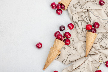 Ripe sweet cherries in waffle cones on light stone concrete background. Flat lay, vintage napkin