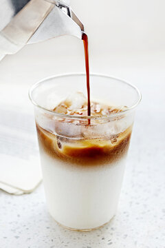 Close-up of coffee being poured into a glass with milk and ice cubes to make an iced latte