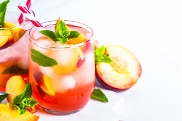 Peach cocktail, iced peach tea, fruit drink, summer beverage with fresh fruits, ice and mint. Close up.