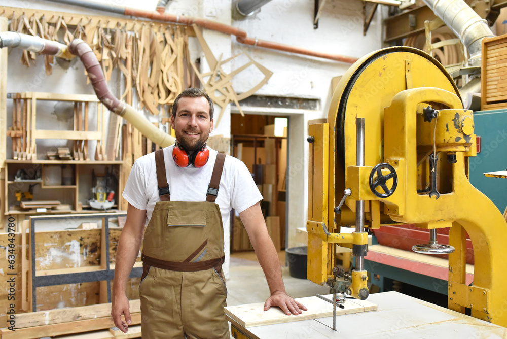 Wall mural portrait of a carpenter in work clothes and hearing protection in the workshop of a carpenter's shop