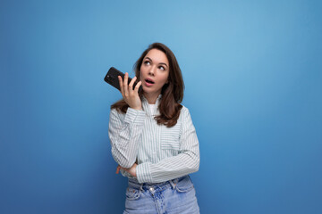 brunette young woman in a shirt typing a voice message in a smartphone on a studio background with copy pace