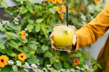 Close-up of a woman standing outdoors holding a green kiwi and basil muddled cocktail
