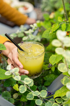 Close-up of a woman standing by plants outdoors holding a green kiwi and basil muddled cocktail