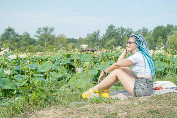 young woman with beautiful blue dreadlocks resting on lotus lake
