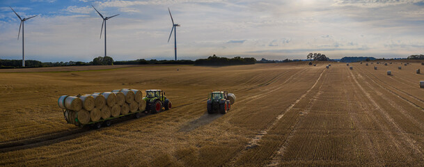 Agricultural panorama scene tractors collecting straw bales in field and loading on tractor...