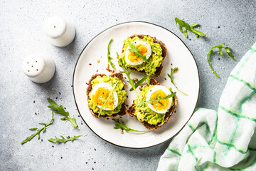 Open sandwich. Whole grain bread with avocado and boiled eggs. Top view on white kitchen table.