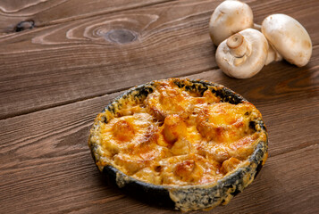 Homemade julienne with cheese and mushrooms . A hot dish with baked cheese crust on a wooden  table.