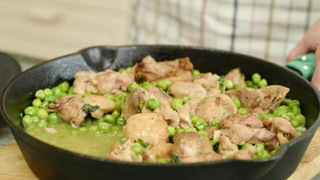 The cook takes the freshly prepared pieces of chicken with peas out of the pan.
