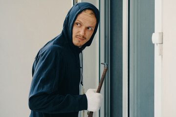 Burglar with crowbar breaking door and looking away