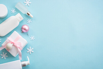 Natural winter cosmetic with holiday decorations and present box on blue background. Winter scincare concept. Flat lay image.