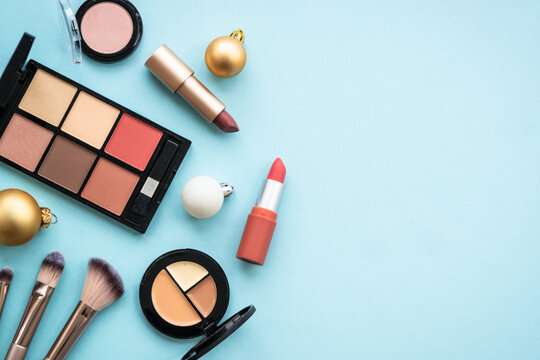 Make up products and christmas decorations on blue background. Holiday shopping. Flat lay image with copy space.