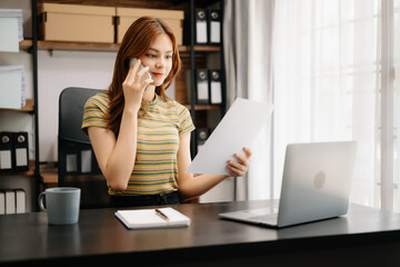 Business asian woman Talking on the phone and using a laptop with a smile while sitting at home office.