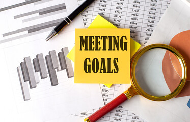 MEETING GOALS text on a sticky on the graph background with pen and magnifier