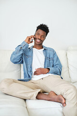 Content black man talking on smartphone on sofa in house