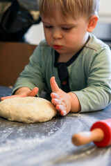Close up of a little boy looking at dough with curiosity, dark grey table