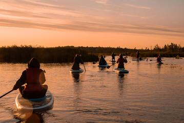 Stand up paddle boarding or standup paddleboarding on quiet lake at sunrise with beautiful colors...