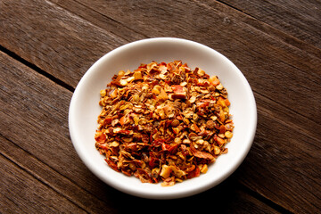 Red Pepper flakes inside a white little dish for seasoning above a wooden table