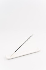 immagine primo piano con bastoncino di incenso profumato e supporto in ceramica bianco, sfondo superficie bianca