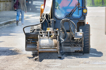 A mounted road mill removes a layer of old asphalt on the roadway.