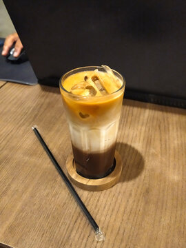 A glass of pretty iced mochaccino coffee and a straw put on the wooden dining table in Asian coffee shop